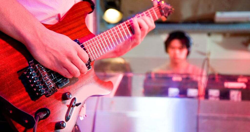 A close up of a guitar player in the foreground and blurred image of a soundengineer in th ebackground to illustrate How Much Does Music Gigs Pay in Dallas