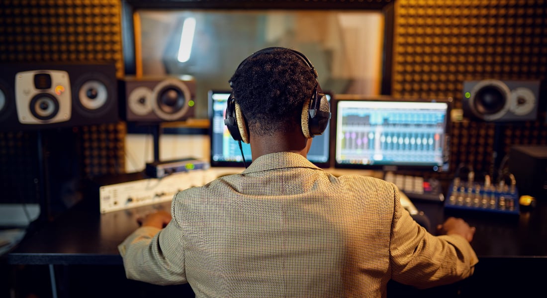 Male sound engineer at mixing console, back view, inside a recording studio