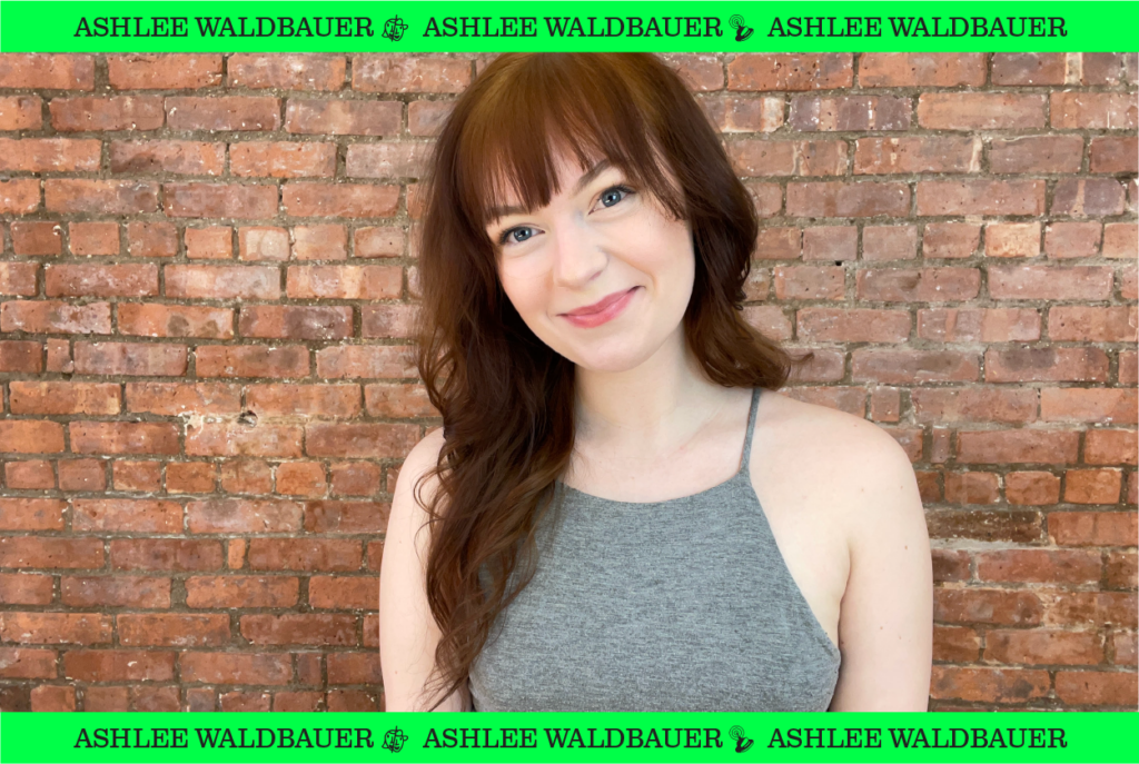 Ashlee Waldbauer standing on front a brick wall.